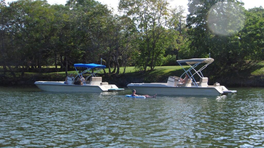 Two rental pontoon boats anchored in a calm cove on a Nashville-area lake with someone floating between them